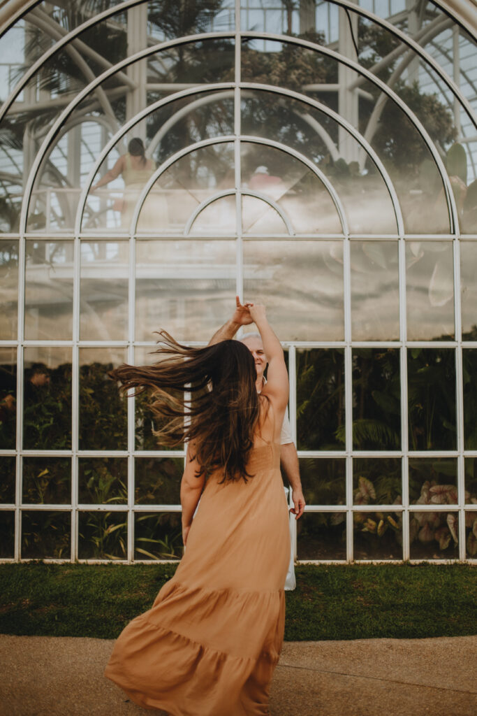 Woman twirling in a flowing dress inside a glass conservatory in Vancouver